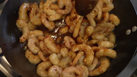 overhead view of frozen prawns being stirred and shaken inside wok with wooden spoon