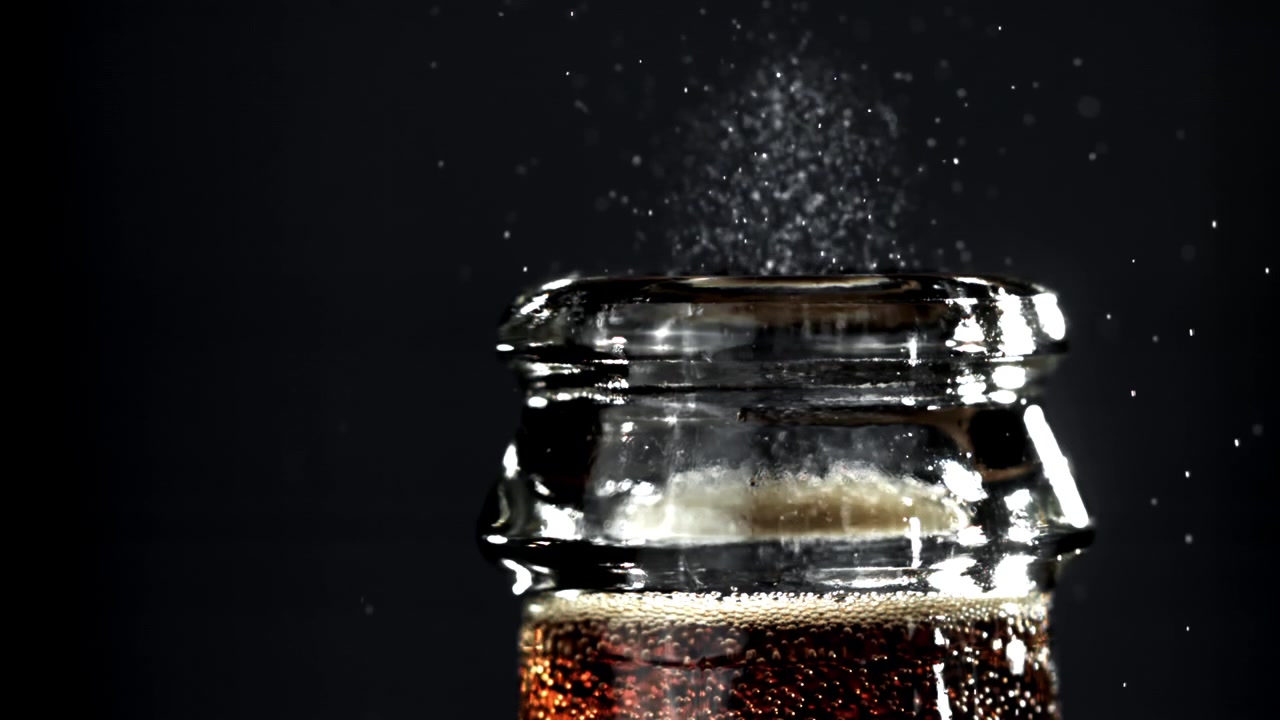 Slow motion di particelle di zucchero che cadono in una bottiglia di cola