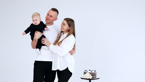 Beautiful Caucasian family with an infant baby. Happy father kisses his son on the cheek. A chocolate cake on the stool beside.