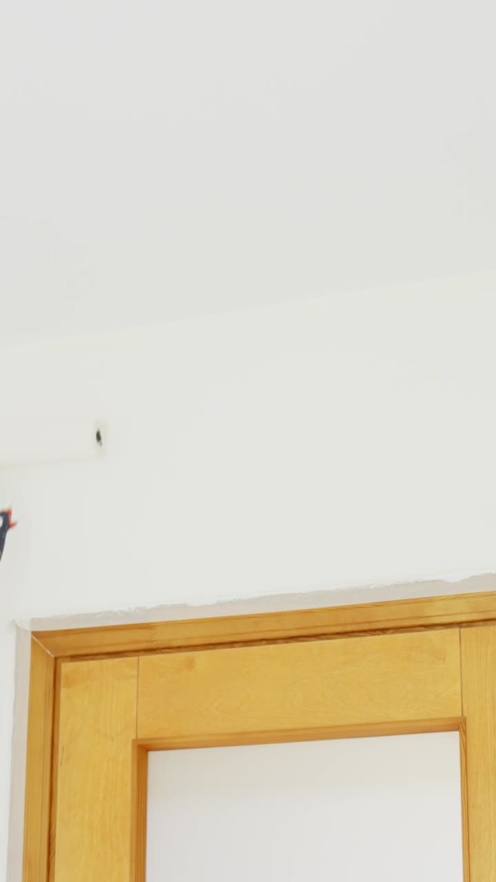 Man painting a white ceiling with a roller on an extension pole, vertical shot