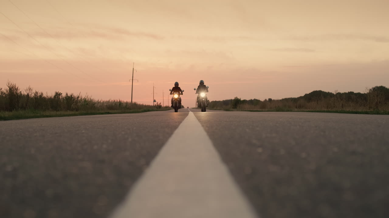 dos motocicletas conducen por una carretera plana al atardecer 1