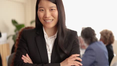 asian woman smiling on camera while working with colleagues inside bank office