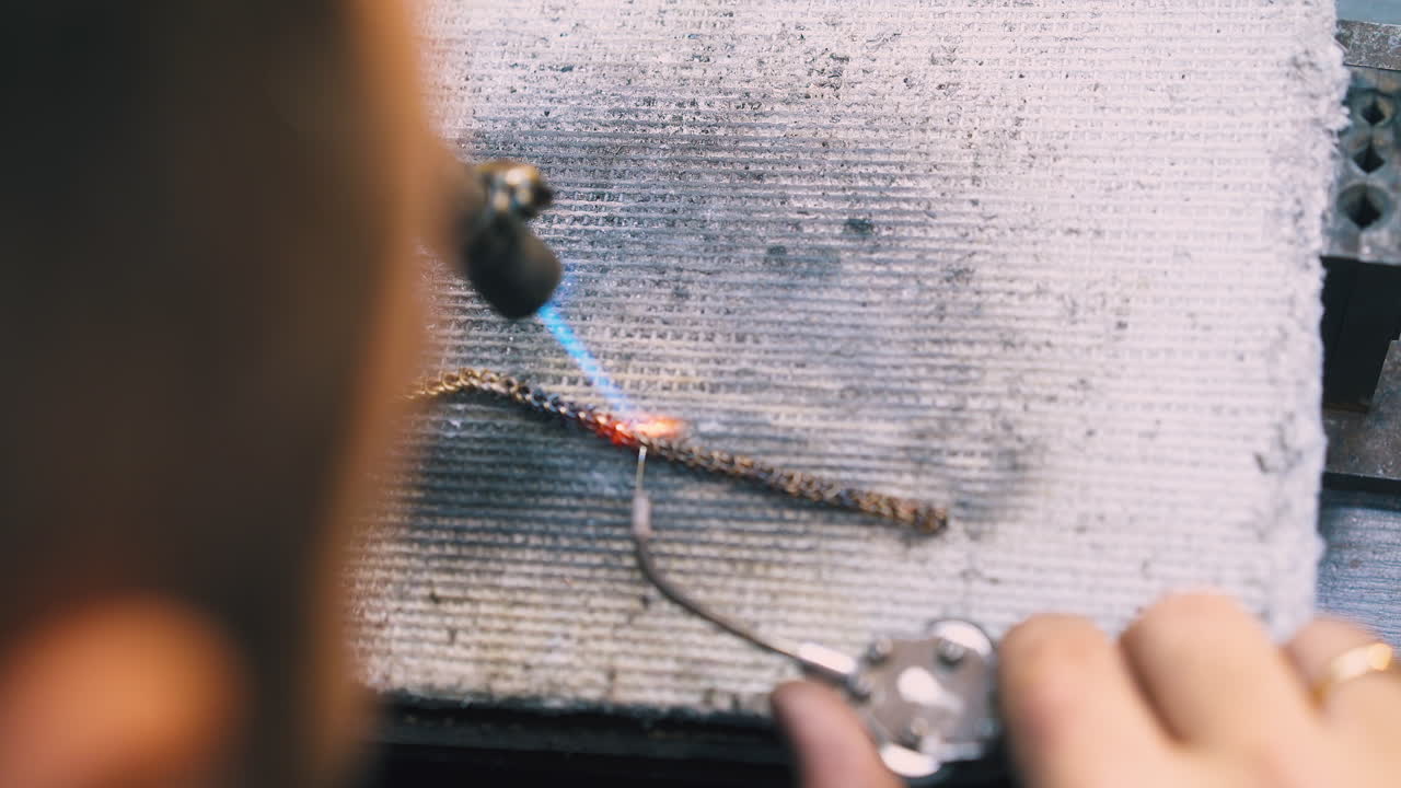 worker welds gold chain with gas burner and tool on sheet