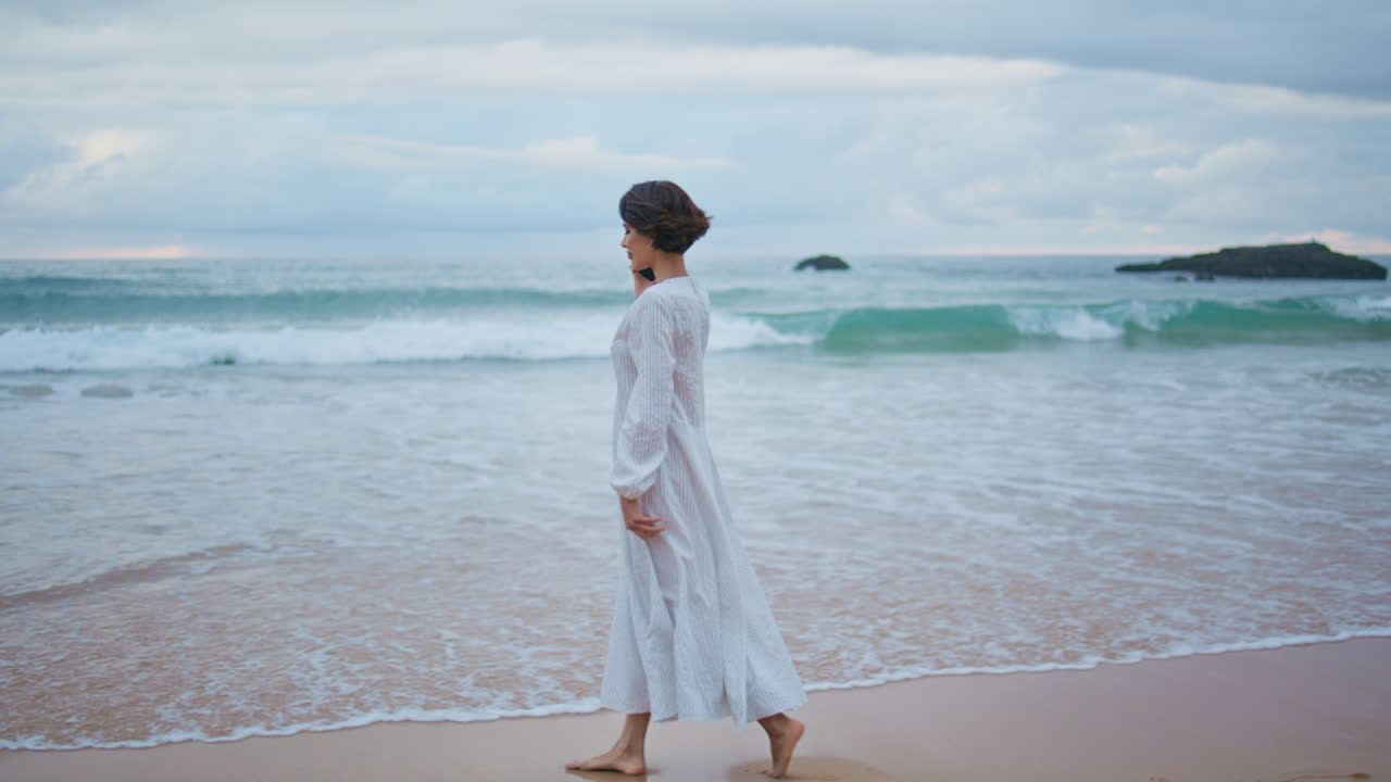 열대 해변에서 휴대전화로 전화하는 여성. 무관심한 모델이 바다의 파도를 고 있다.