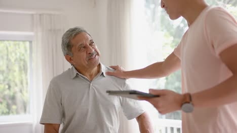 diverse male physiotherapist with tablet shaking hands with senior male patient, in slow motion