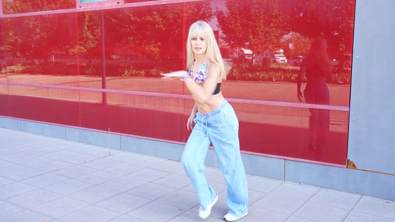 A young woman wearing stylish casual clothes dancing energetically outdoors in an urban city setting