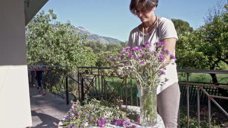 Woman-decorates-a-vaze-with-wildflowers-at-a-porch-of-a-countryhouse-60fps