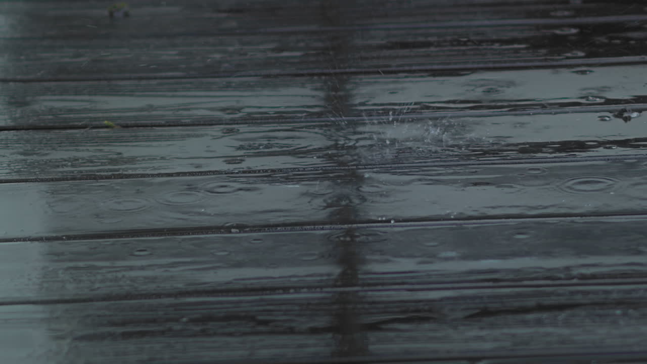 Rain drops fall and splatter on wooden deck, close up