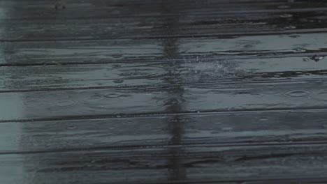 rain drops fall and splatter on wooden deck, close up