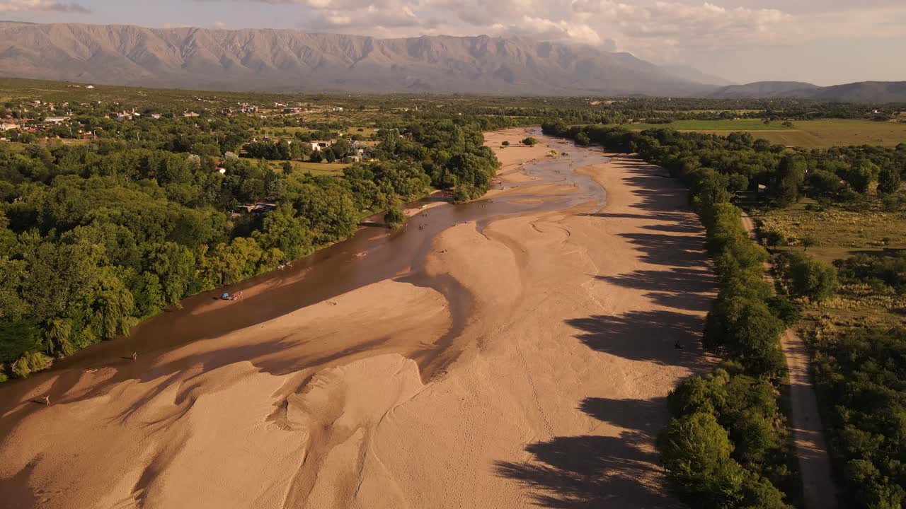 vista aérea del río seco rodeado de árboles verdes y cordillera en el fondo - clima cálido en argentina