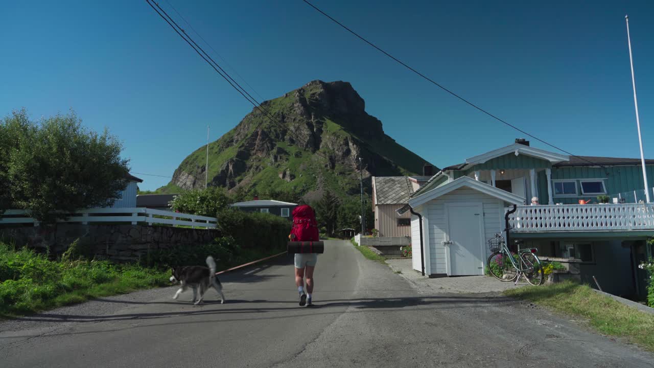 목줄에 개 애완동물을 둔 사람이 노르웨이 노르드랜드 로번트에 있는 평화로운 마을의 길을 걷고 있습니다.