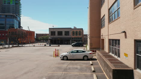 Footage-of-alone-white-passenger-car-staying-on-parking-lot-in-town-from-drone-softly-landing-at-asphalt-drone.-Dallas,-Texas,-US