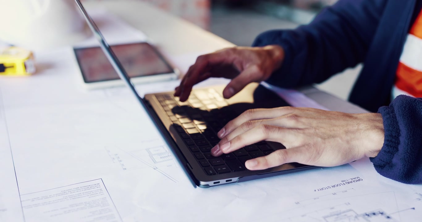Architect Working on Laptop with Blueprints in Construction Site