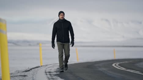 a warmly dressed traveler walks alone on a remote road, surrounded by the vast, snow-covered mountains of an icelandic winter landscape