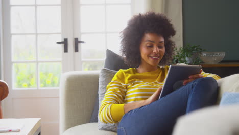 Woman-Relaxing-On-Sofa-At-Home-Using-Digital-Tablet-To-Stream-Movie-Or-Shop-Online