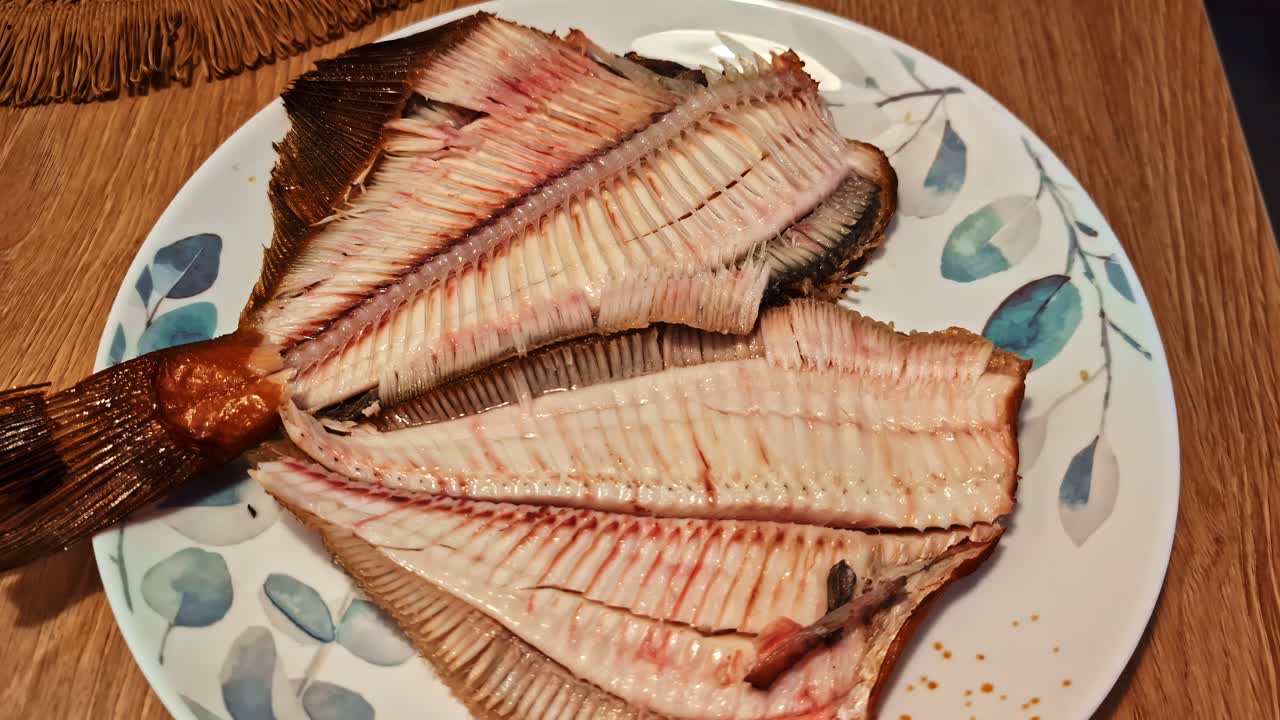 Close-up of a cooked and filleted flatfish with its spine and bones visible, prepared for a delicious meal on a decorative plate - push in