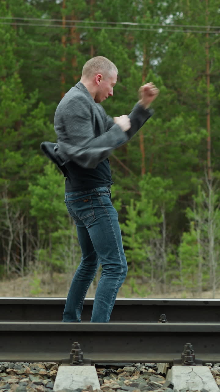 숲 속 의 철도 트랙 을 따라 태권도 를 연습 하고 있는 회색 의복 재 과 파란 청바지 를 입은 남자