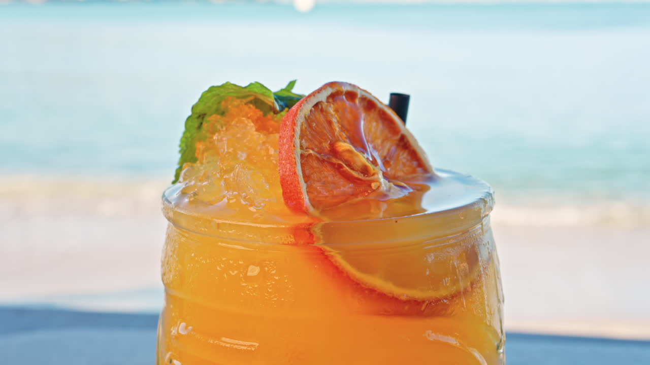 Close up of an orange cocktail on a table with a blurred view of the sea on the background