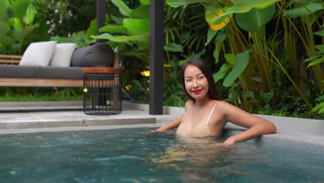 happy asian woman in skin toned bikini enjoying in a luxurious swimming pool in a modern tropical outside spa area, medium shot with copy space