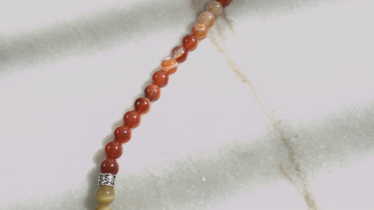 Sliding shot of red jasper beads in a prayer mala placed on a white marble slab shot in UHD 4K