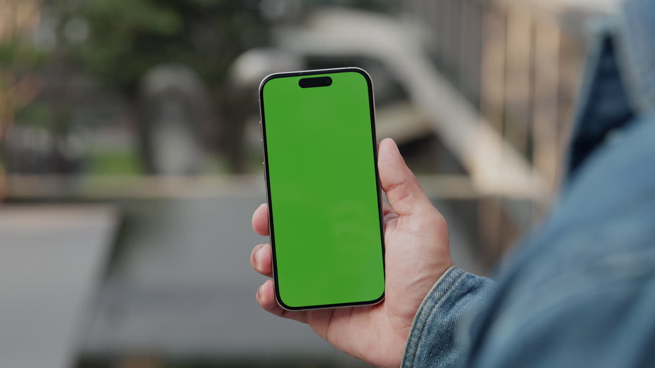 Persona che tiene in mano uno smartphone con schermo verde all'aperto