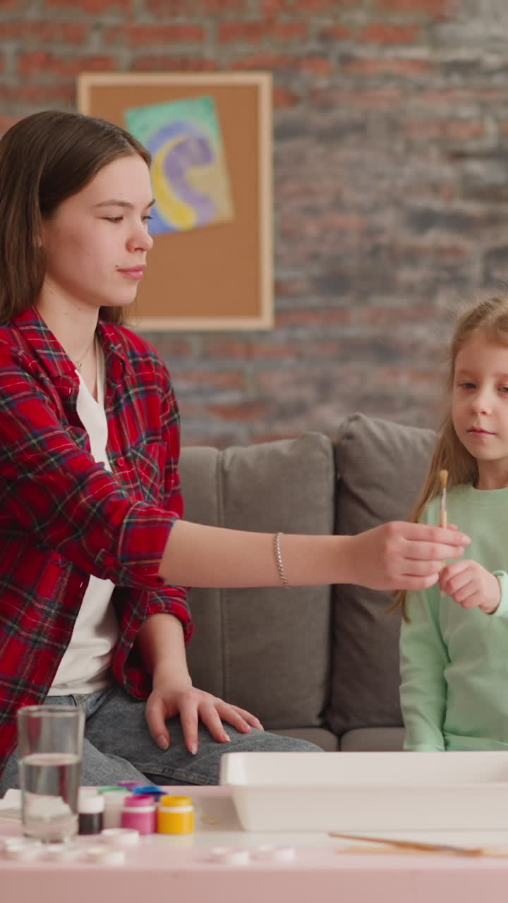 la niña le da un pincel a la hermana mayor pensativa que se prepara para el dibujo de ebru en la mesa en la sala de estar. los niños pasan tiempo juntos. hobby y ocio