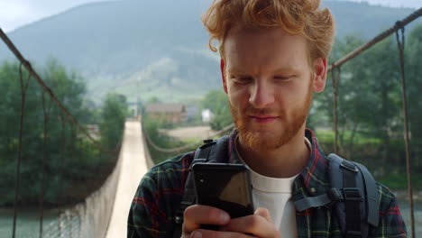 Hitchhiker-texting-mobile-phone-at-mountains.-Smiling-guy-read-news-outside.