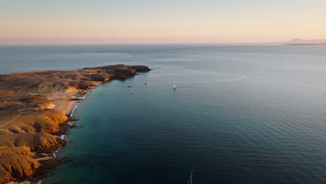 Stunning Drone Flight Over Lanzarote's Playa Mujeres with Sailboats and Fuerteventura in the Background During Beautiful Sunset