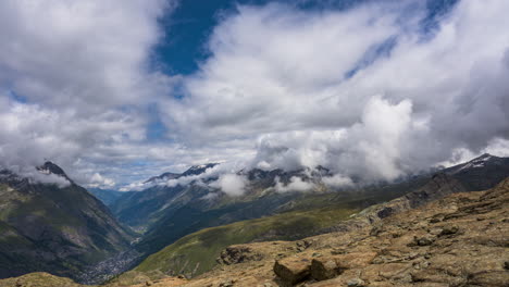 timelapse of thick clouds soaring over the zermatt village in switzerland with patches of fog on a sunny day - high angle shot