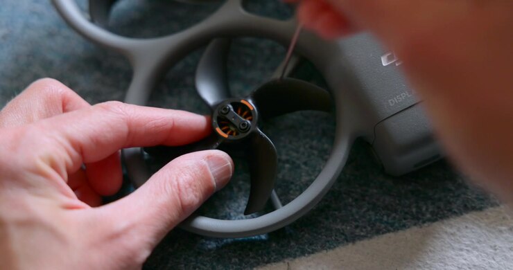 Primo piano di mani attente che regolano un motore di drone FPV e una protezione dell'elica su una superficie di lavoro per riparazione o manutenzione.