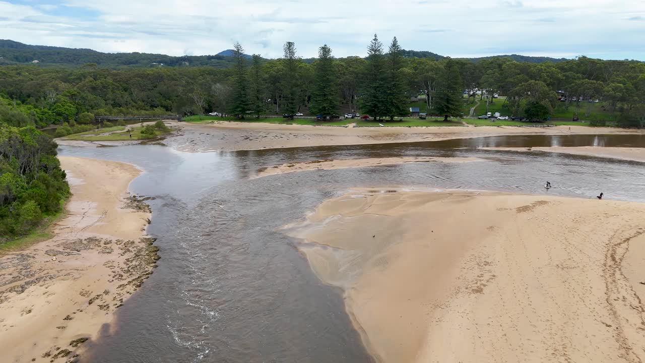 Drone pans over winding river, sandy banks, and lush trees at Moonee Beach