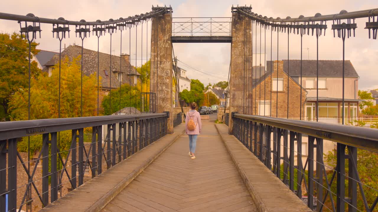 A Woman Crossing The Old Bono Suspension Bridge In Le Bono, Brittany, France. Wide Shot