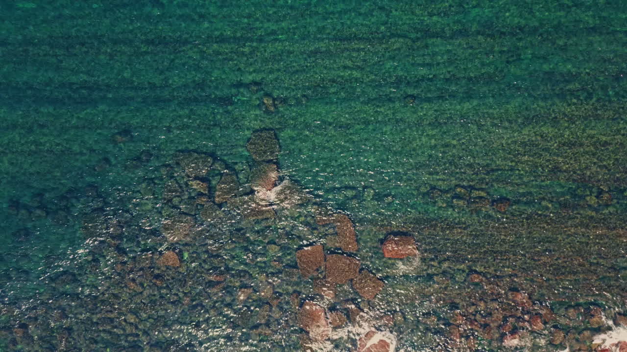 Kıyı taşlarına çarpan şeffaf deniz suyu, yukarıdan görünüm. Taşlara vuran dalgalar.