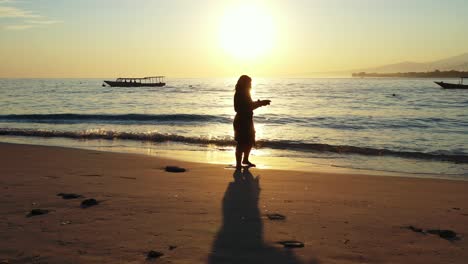 Una-Mujer-Tomando-Una-Foto-En-La-Orilla-Bajo-La-Sombra-De-Una-Brillante-Puesta-De-Sol-En-La-Playa-De-Krabi---Toma-Amplia