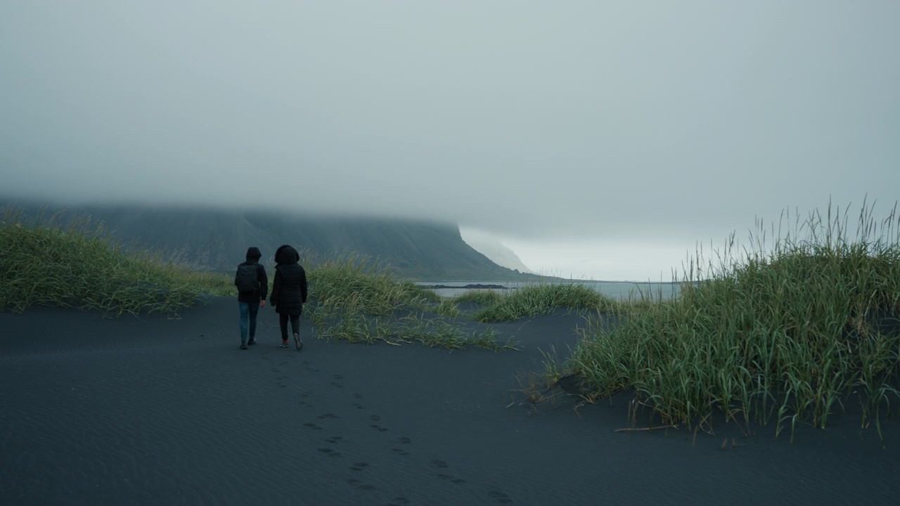 Couple walking on foggy Stokksnes Beach with Vestrahorn, black sand scene