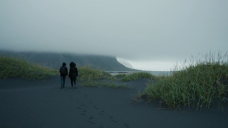 Couple walking on foggy Stokksnes Beach with Vestrahorn, black sand scene