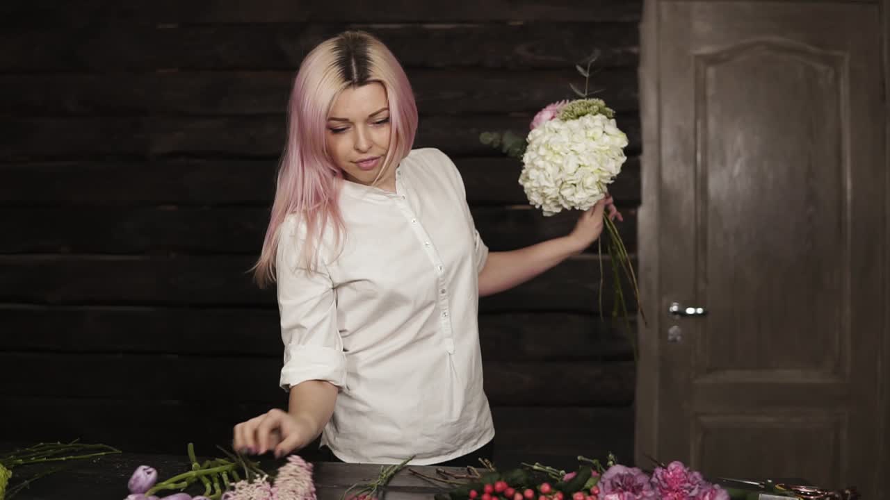 передний вид нежной, молодой девушки в белой рубашке, устраивающей цветок за цветом в букете.
