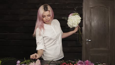 Front-view-of-a-tender,-young-girl-in-white-shirt-arranging-flower-by-flower-in-bouquet.-Indoors