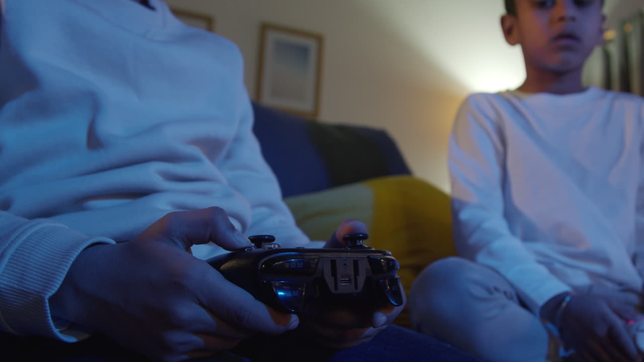 cerca de las manos de dos niños jóvenes en casa jugando con consola de juegos de computadora en la tv sosteniendo controladores a última hora de la noche 6
