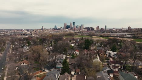 Una-Toma-Aérea-Inclinada-Hacia-Arriba-Del-Horizonte-De-Minneapolis-En-Minnesota-En-Un-Día-De-Primavera-Con-Casas-Suburbanas-En-Primer-Plano