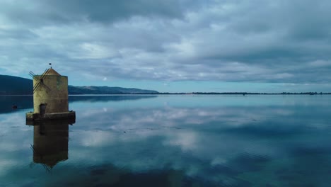 Old-Spanish-Mill-in-the-lagoon-at-the-island-town-Orbetello-close-to-Monte-Argentario-and-the-Maremma-Nature-Park-in-Tuscany,-Italy,-with-blue-sky-and-calm-blue-water