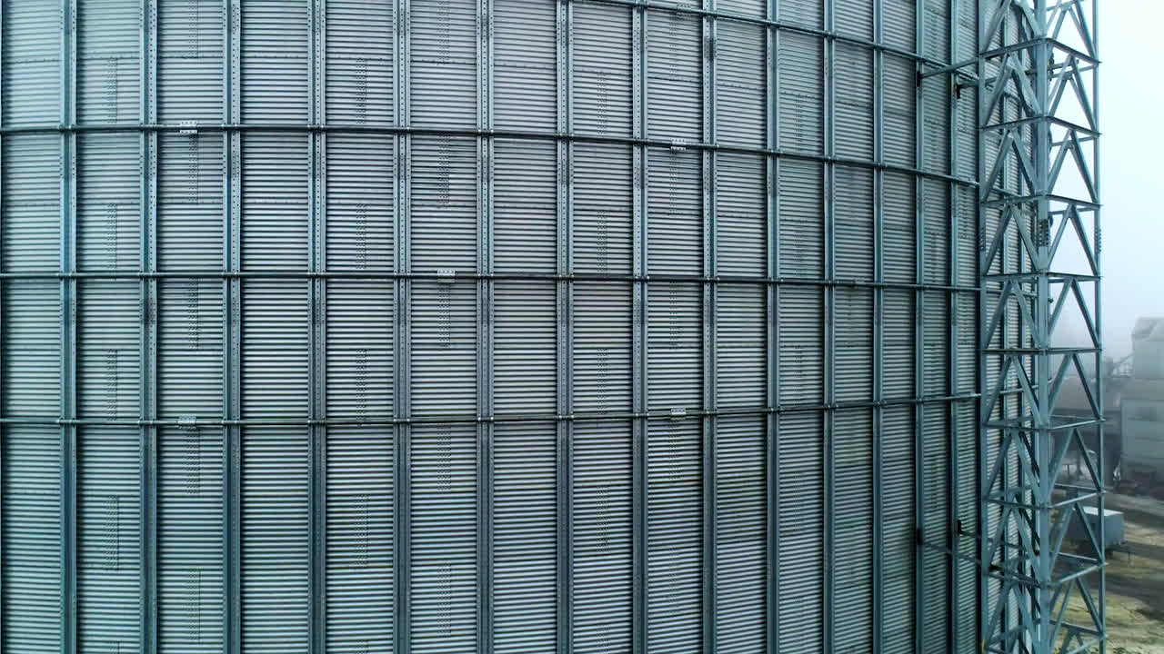 Metal surface of huge elevator container. Rising along the silver shell of granary tank up to the top. Foggy sky backdrop.