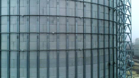 metal surface of huge elevator container. rising along the silver shell of granary tank up to the top. foggy sky backdrop.