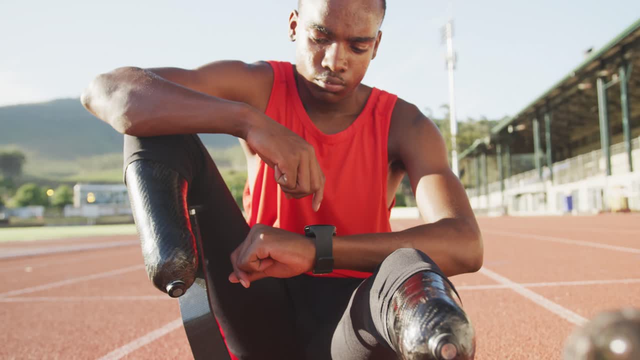 Disabled mixed race man with prosthetic legs sitting on racing track