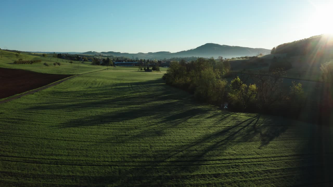 aerial drone view of morning hour over peaceful countryside with green and agricultural fields, sun shining directly into camera, switzerland