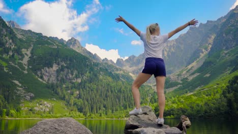 Bella-Chica-Posando-En-Un-Hermoso-Lago-De-Montaña-Con-árboles-Verdes-Y-Cielo-Azul-Con-Vistas-A-La-Montaña