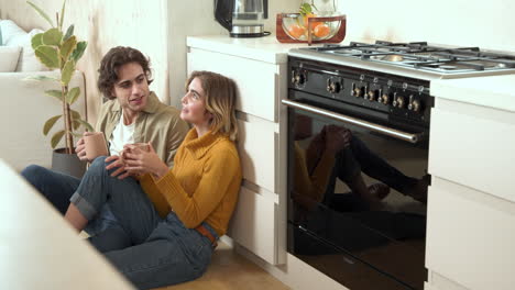 couple enjoying hot drinks together on kitchen floor, sharing cozy moments