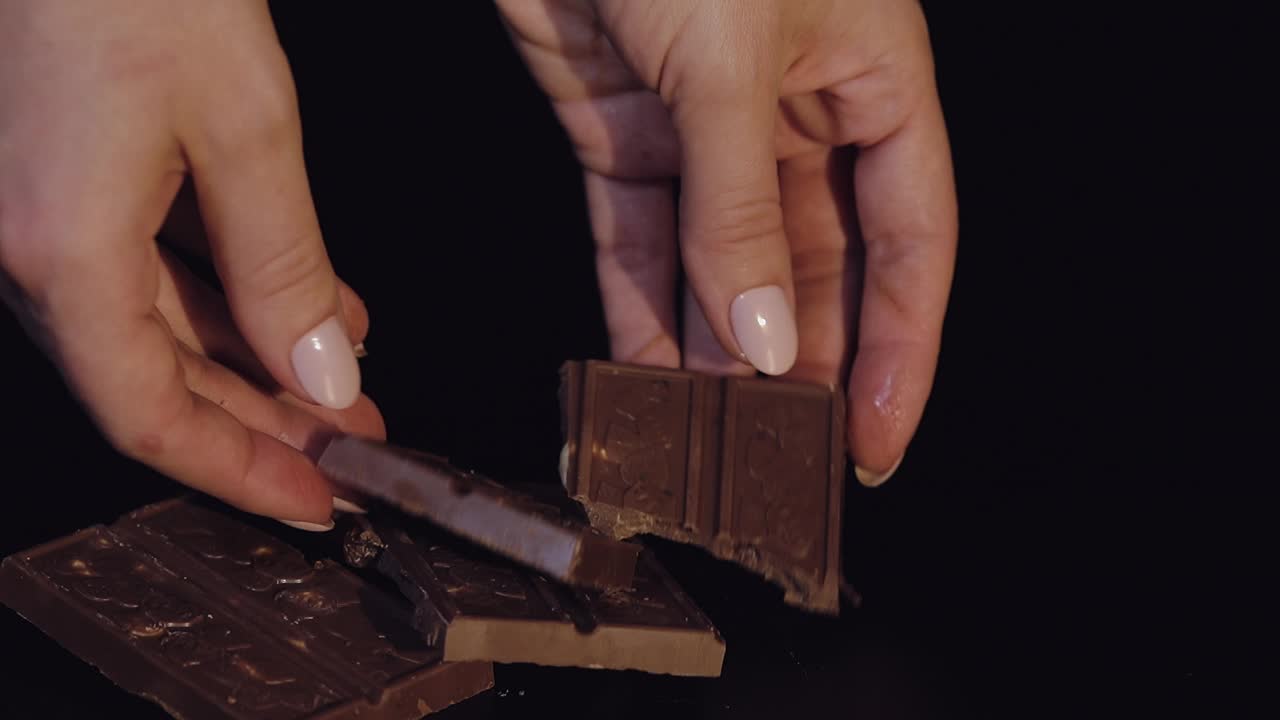 mujer rompe una barra de chocolate negro con nueces. primer plano. cámara lenta