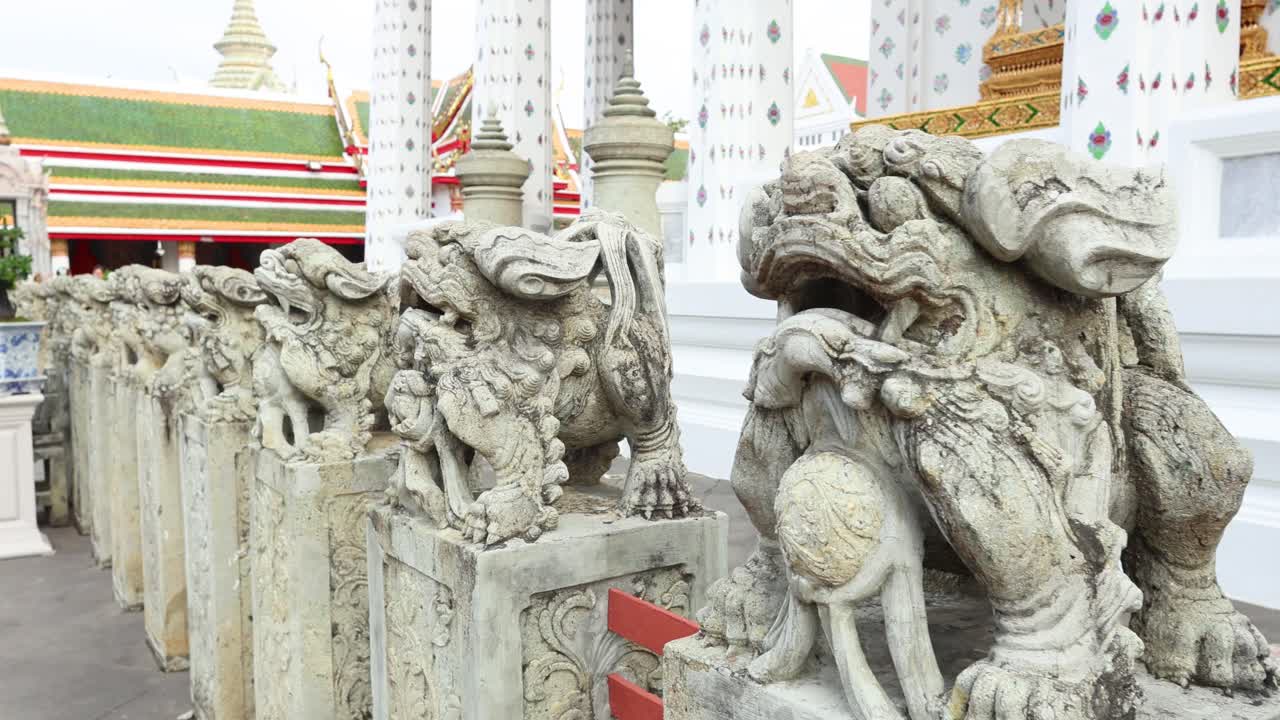 Detailed view of intricate stone lion statues lining a pathway at Wat Arun, Bangkok. Bright daylight enhances the temple's ornate architecture