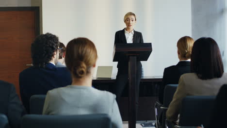 caucasian businesswoman speaker on a podium at a conference and interacting with people in the hall during her speech